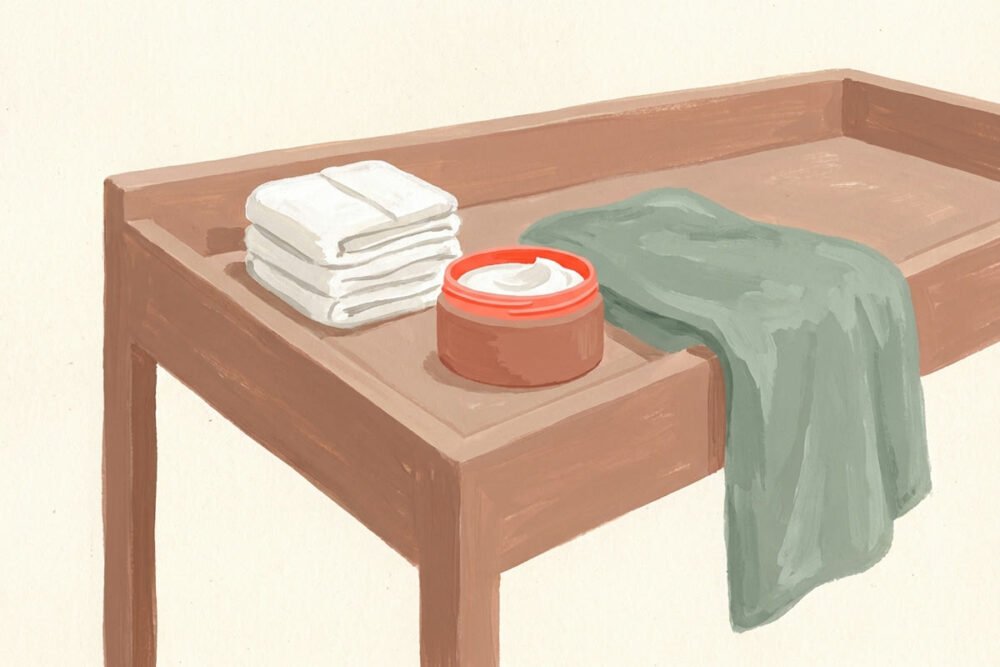 Gouache illustration of a changing table with a stack of folded diapers, an open jar of white barrier cream, and a green towel