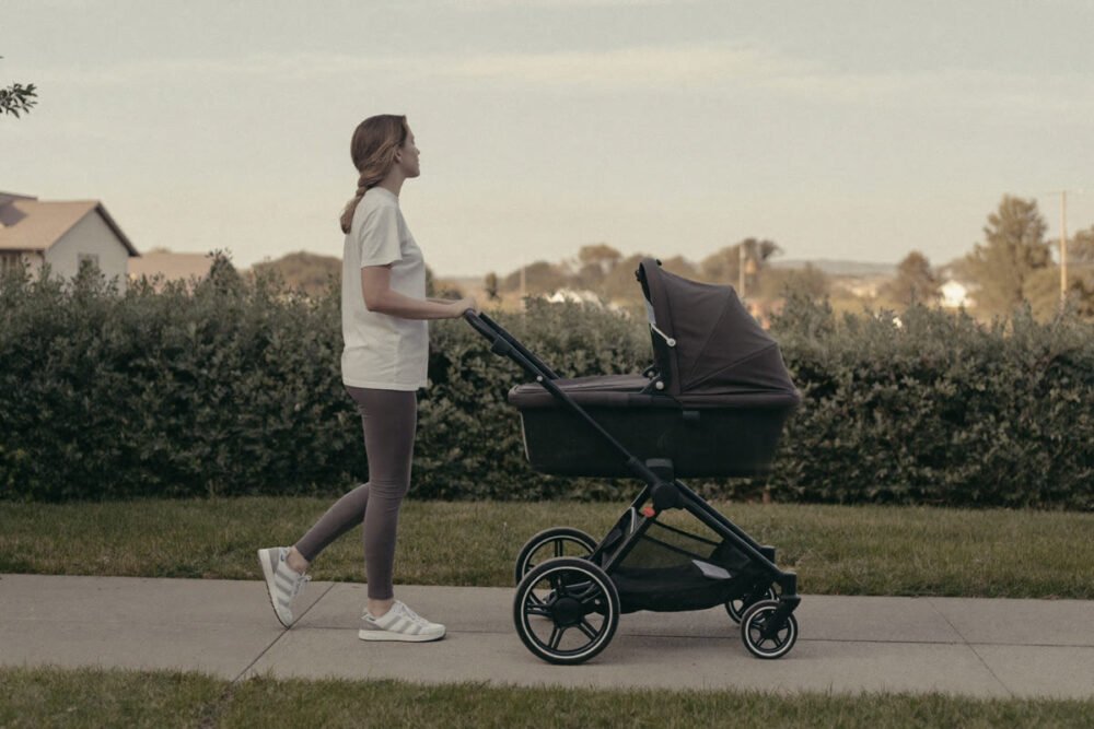 Woman in a t-shirt and leggings pushing a stroller past a hedge on a suburban sidewalk