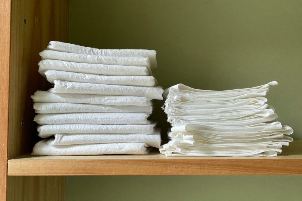 Bathroom shelf with a stack of thick maternity pads next to a smaller stack of thin everyday liners, showing the size difference.